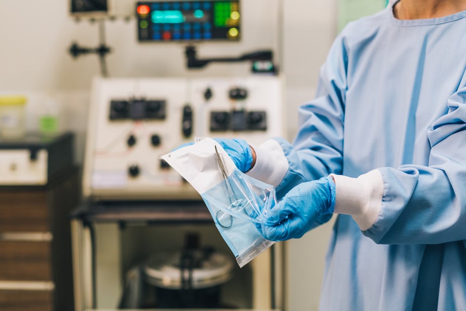 medical-professional-in-scrubs-unwraps-sterile-forceps